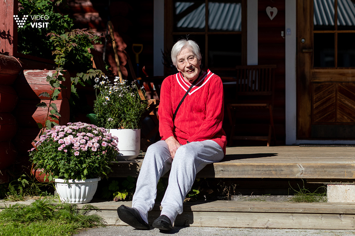Marjatta istuu ulkorappusilla kukkien vieressä.